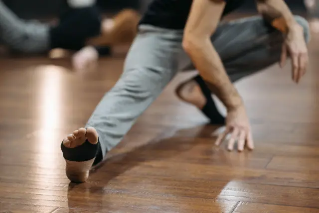 A person seated on the floor of a home living room, mid-stretch, calm and focused.