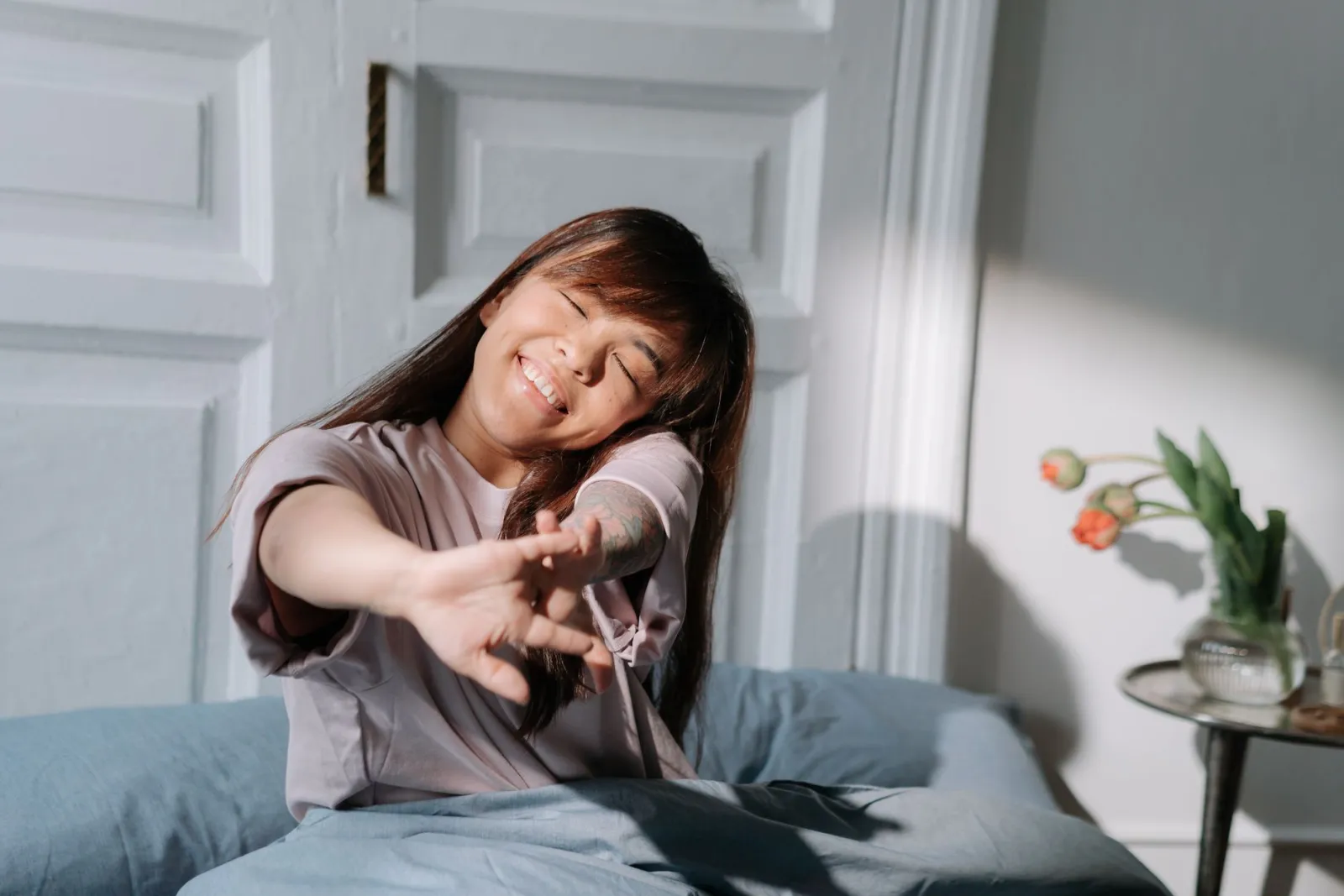 A smiling woman stretching after waking up in bed.