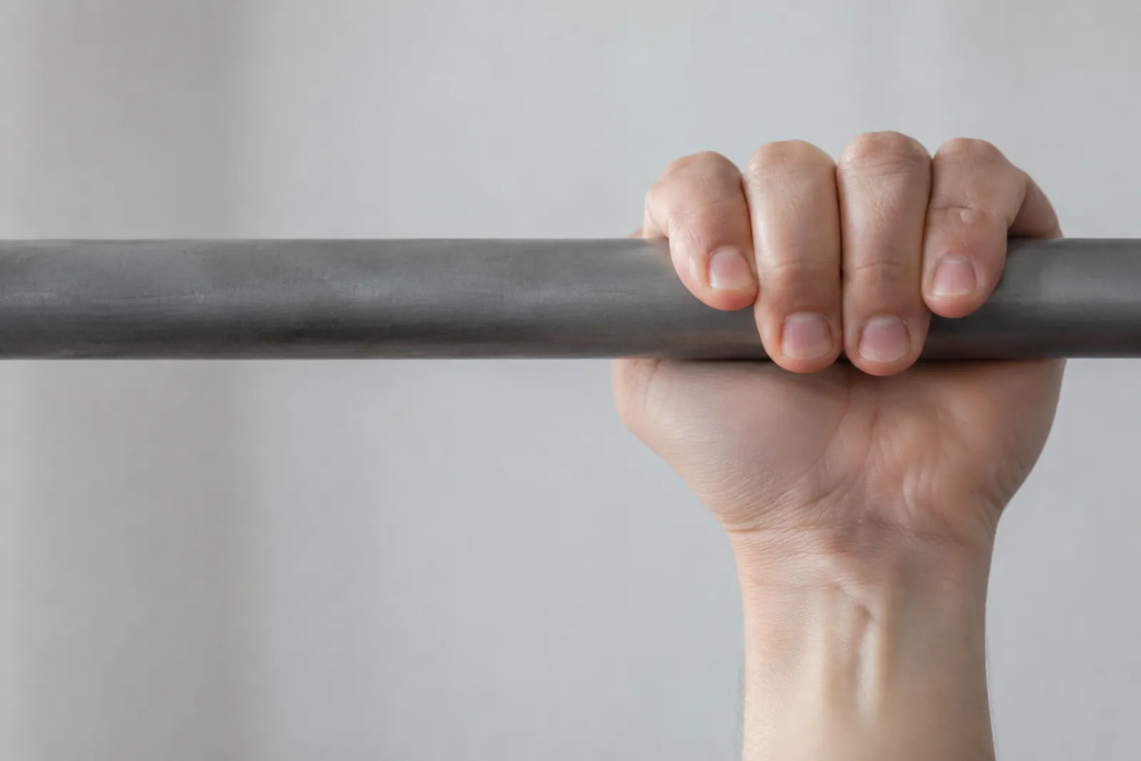 A close view of a hand gripping a barbell in a plain indoor setting.