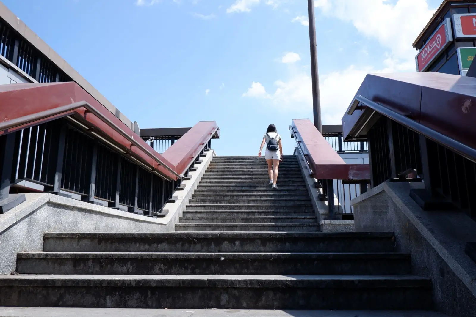 A woman with a backpack climbing a long flight of concrete steps under a clear blue sky.