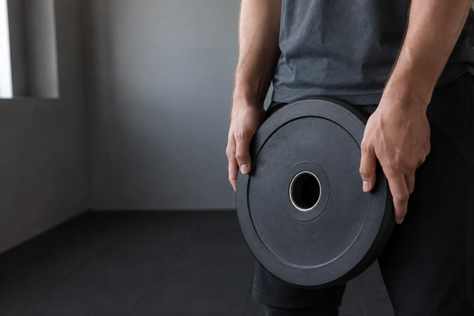 A close view of a person holding a weight plate in a plain indoor space.