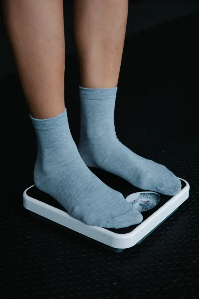 A close-up of feet in gray socks standing on a bathroom scale, dim light.
