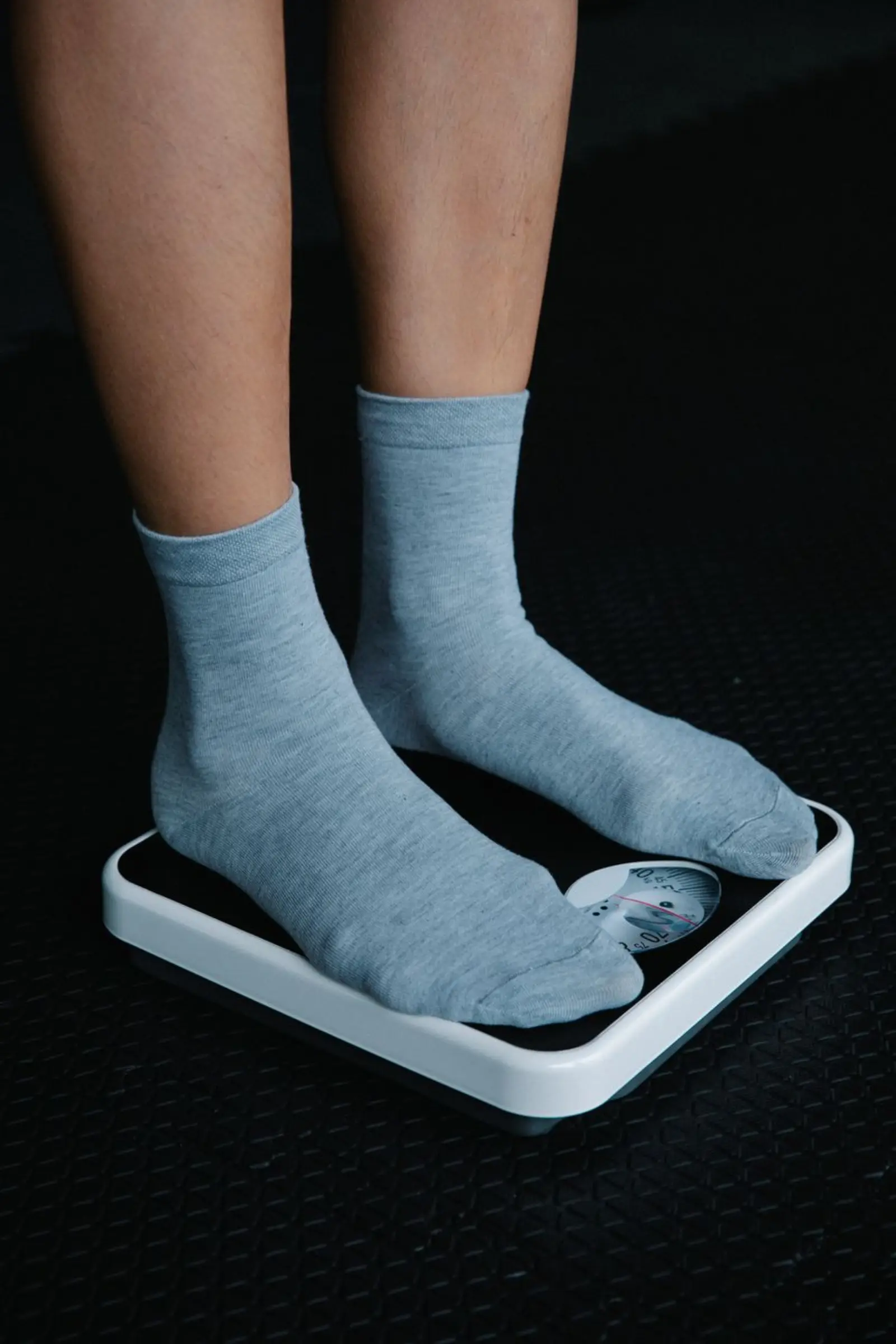 A close-up of feet in gray socks standing on a bathroom scale, dim light.