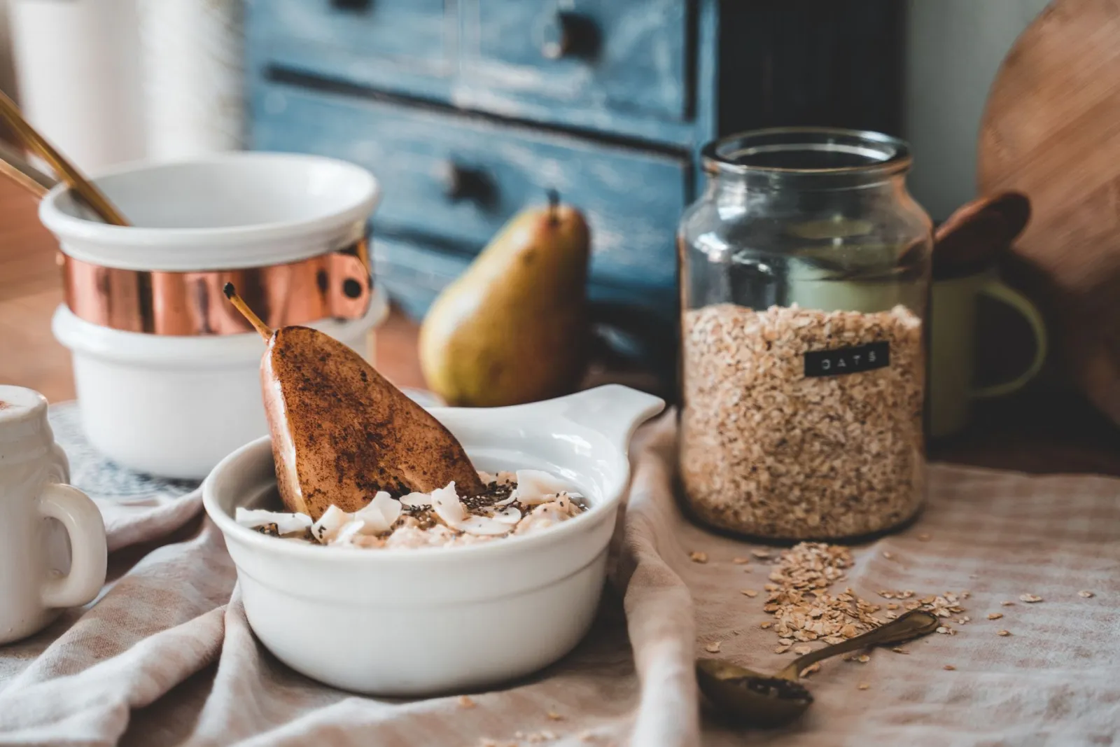 A bowl of oats with sliced pear on a rustic kitchen table in soft morning light.