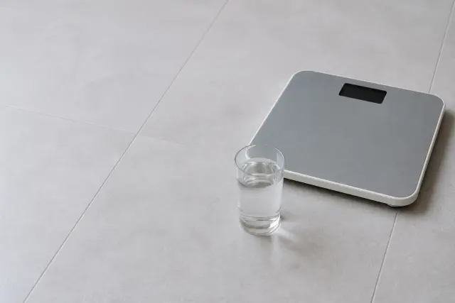 A glass of water and a bathroom scale on a tiled floor in flat morning light.