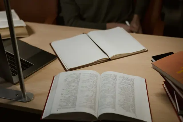An open journal article beside a laptop and notebook on a wooden desk.