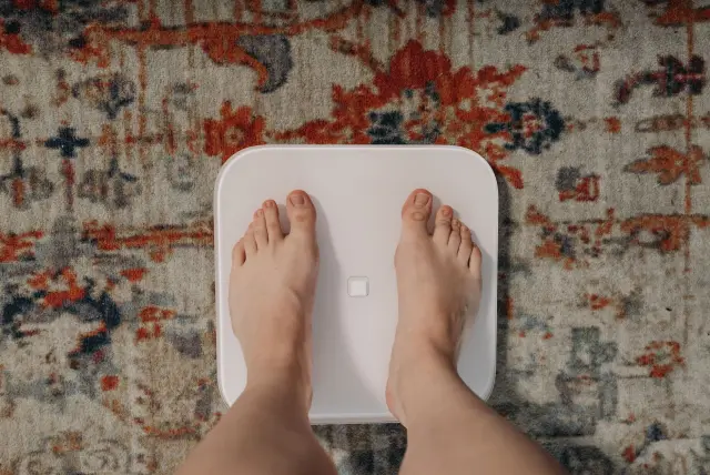 Feet standing on a smart bathroom scale placed on a patterned rug.