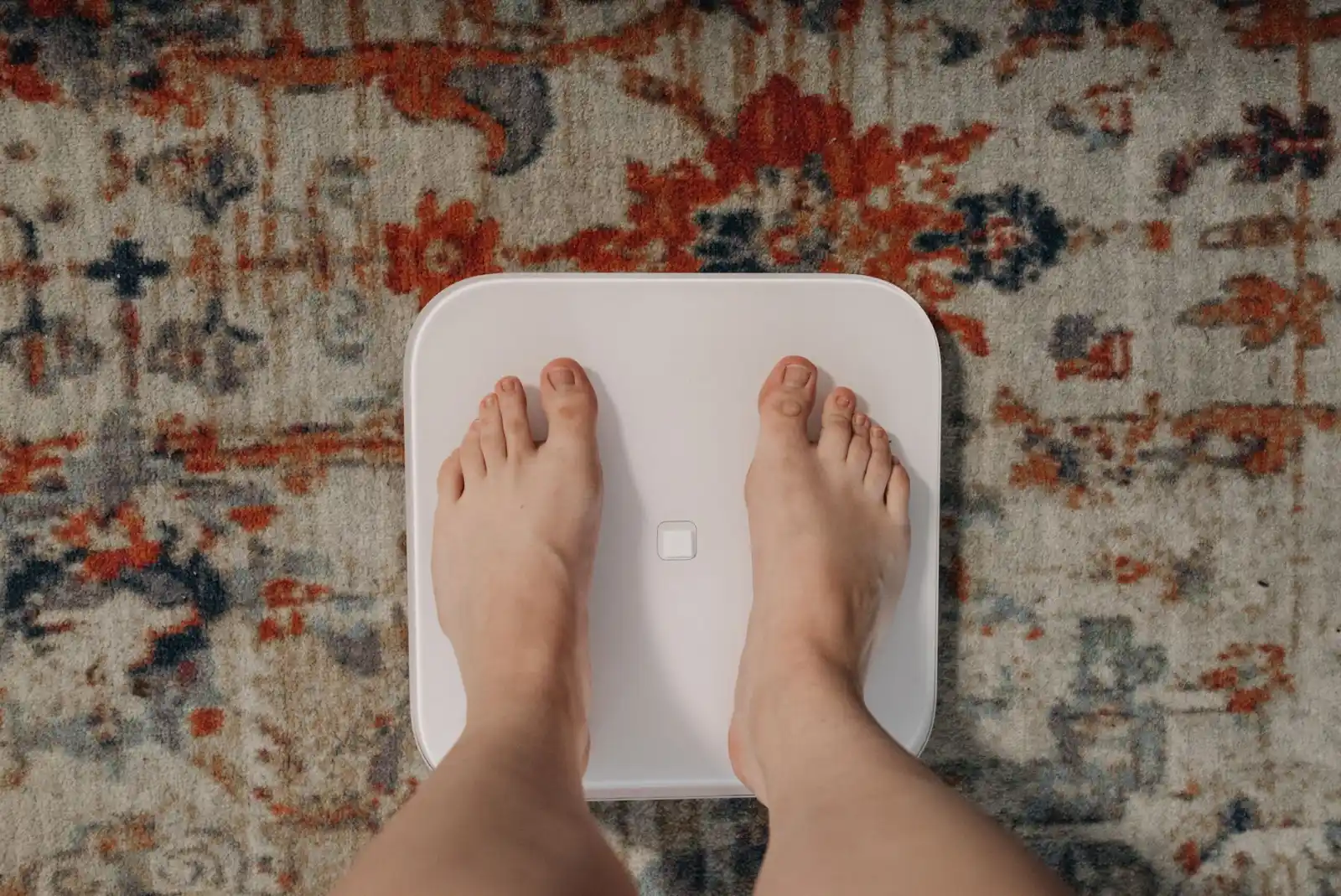 Feet standing on a smart bathroom scale placed on a patterned rug.