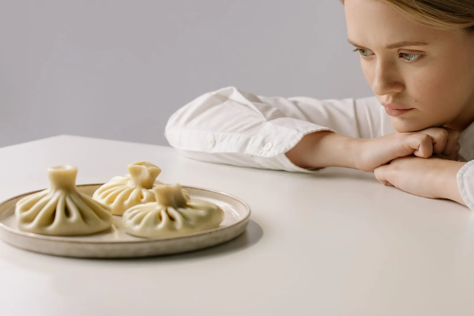 A woman seated alone at a dinner table, gazing thoughtfully at a plate of food without eating.