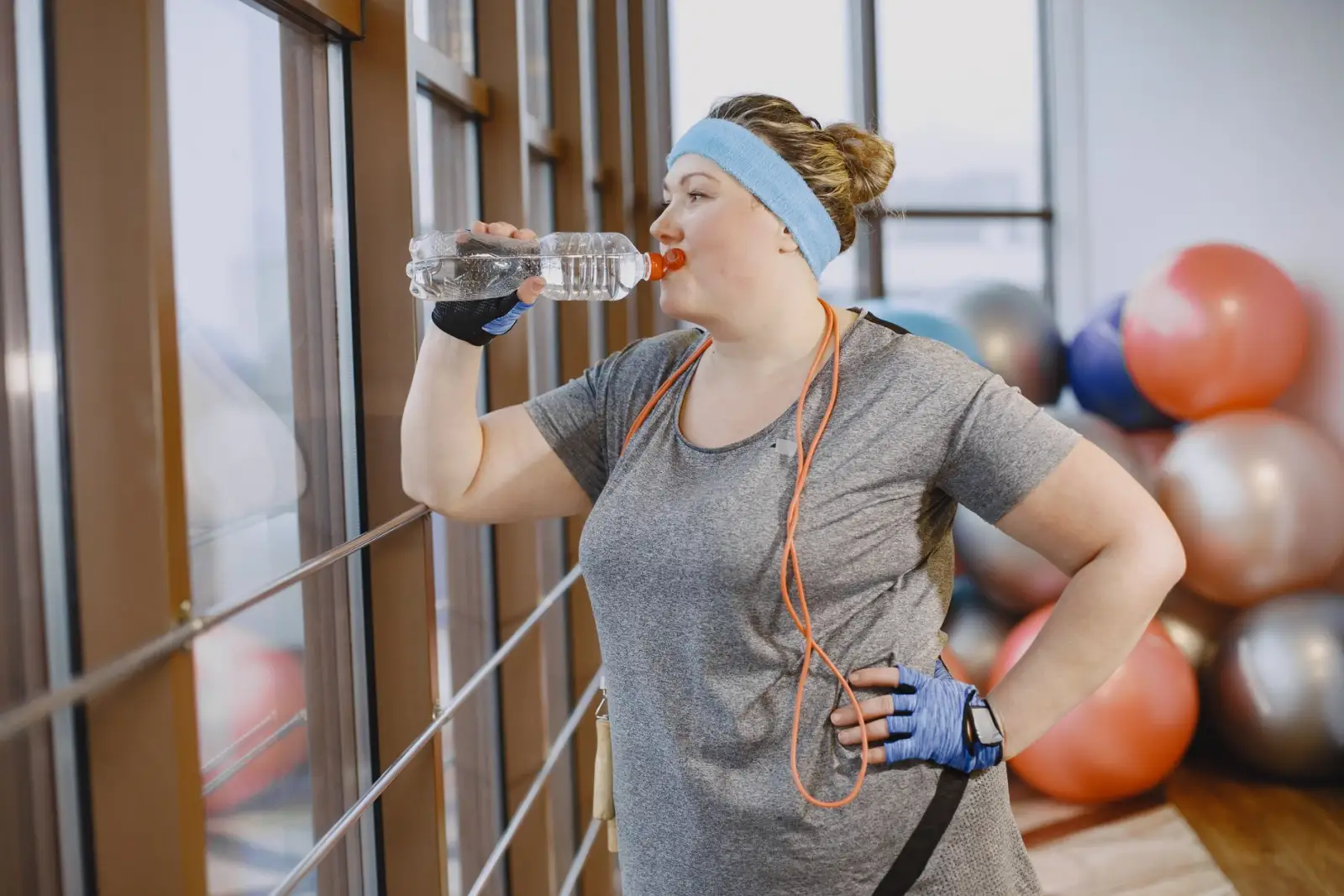 A woman pausing mid-session in a bright gym to drink from a water bottle.