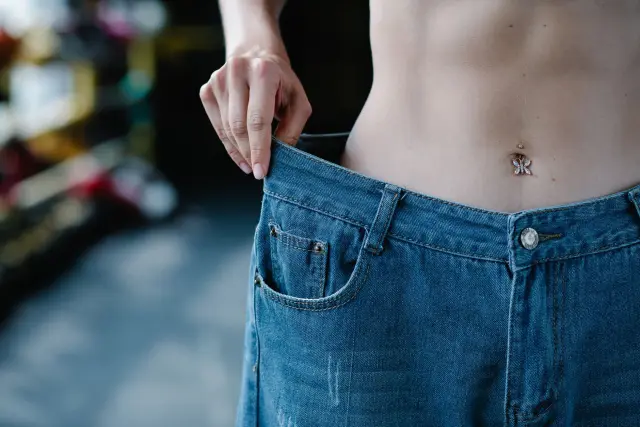 Close-up of a woman pulling at the loose waistband of her jeans.