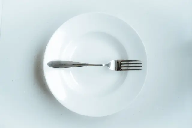 A single fork resting on an empty white plate against a plain background.