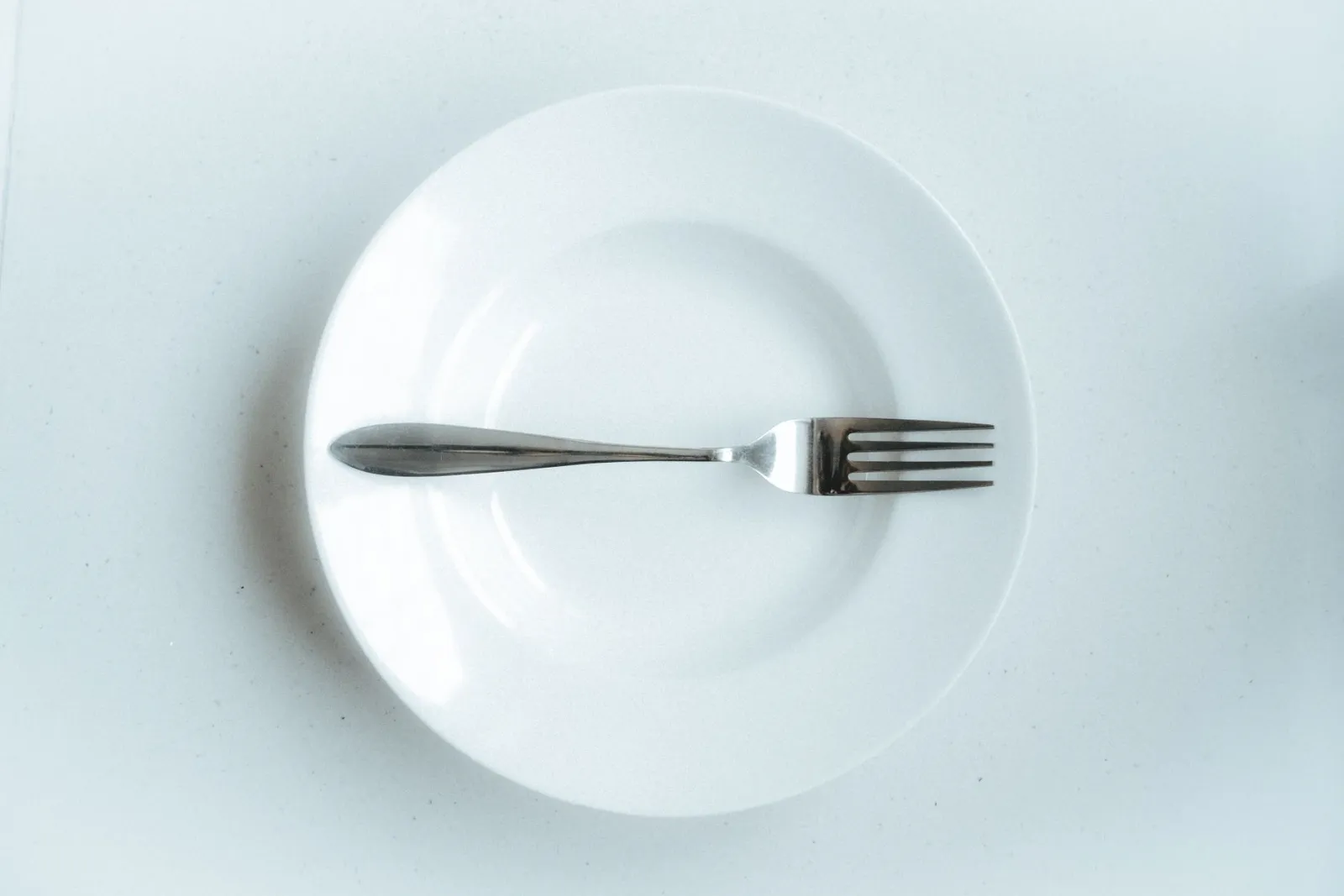A single fork resting on an empty white plate against a plain background.