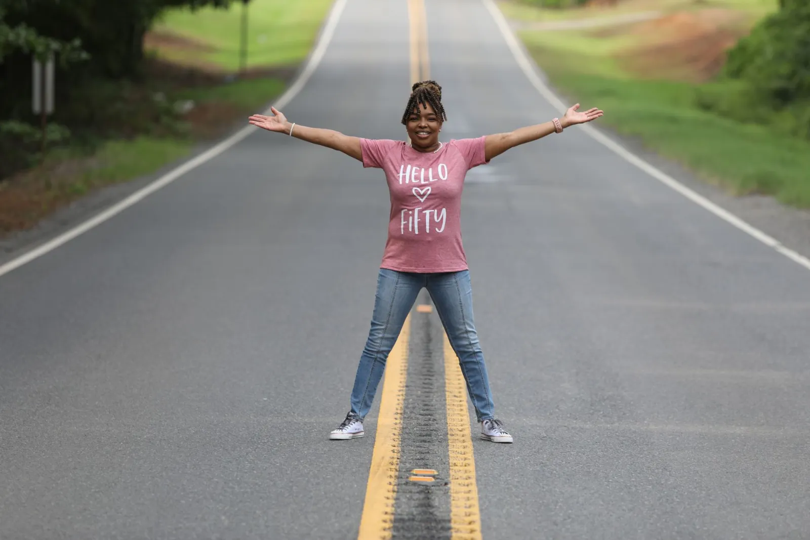 A cheerful woman celebrating a milestone birthday on a quiet rural road.